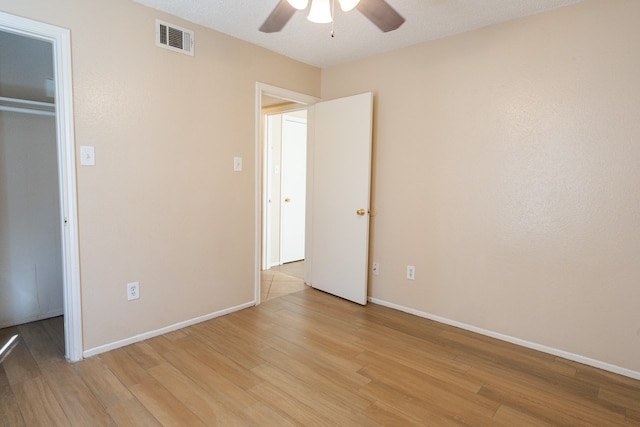 unfurnished bedroom featuring a spacious closet, ceiling fan, a textured ceiling, a closet, and light wood-type flooring