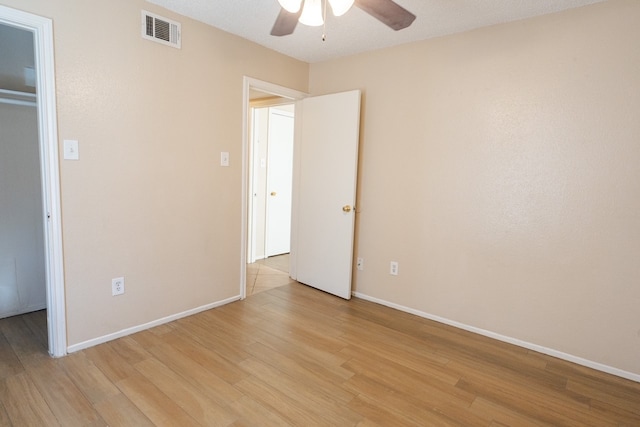 unfurnished bedroom with ceiling fan, a spacious closet, a textured ceiling, a closet, and light wood-type flooring