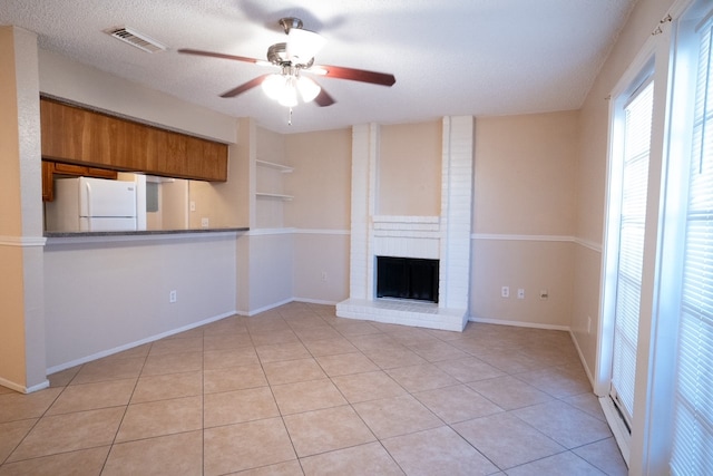 unfurnished living room with ceiling fan, light tile patterned flooring, a textured ceiling, and a brick fireplace