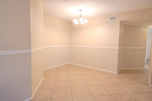 tiled empty room featuring a textured ceiling and an inviting chandelier