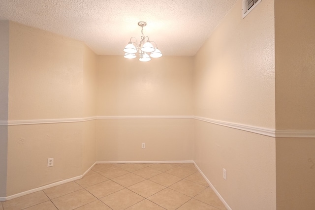 tiled spare room featuring a textured ceiling and a notable chandelier