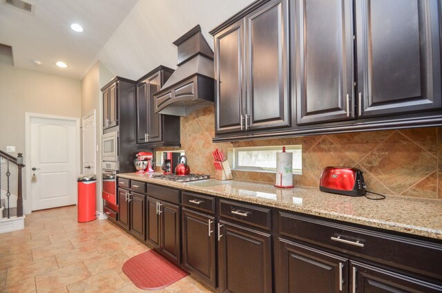 kitchen featuring light stone countertops, backsplash, premium range hood, and stainless steel appliances