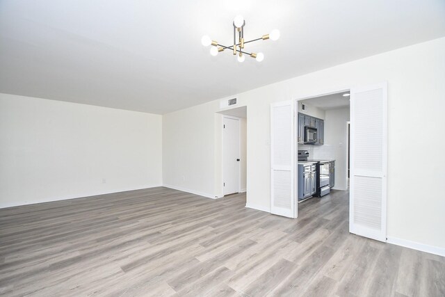 unfurnished living room featuring an inviting chandelier and light hardwood / wood-style flooring