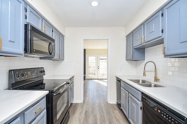 kitchen with black appliances, decorative backsplash, sink, and light hardwood / wood-style flooring