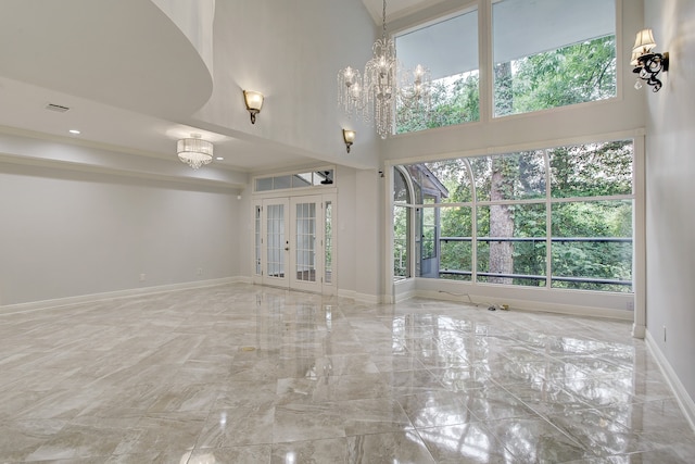 unfurnished living room with a notable chandelier, a towering ceiling, and french doors