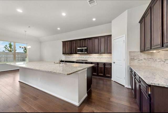 kitchen featuring light stone counters, a kitchen island with sink, decorative light fixtures, a notable chandelier, and dark hardwood / wood-style floors