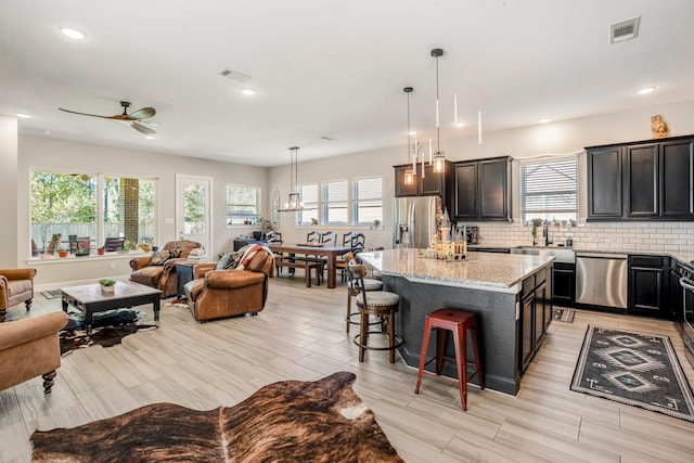 kitchen with light stone countertops, appliances with stainless steel finishes, sink, decorative light fixtures, and a center island