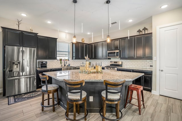 kitchen featuring a center island, light stone countertops, appliances with stainless steel finishes, hanging light fixtures, and a kitchen breakfast bar