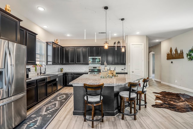 kitchen with appliances with stainless steel finishes, a kitchen island, sink, hanging light fixtures, and light stone counters