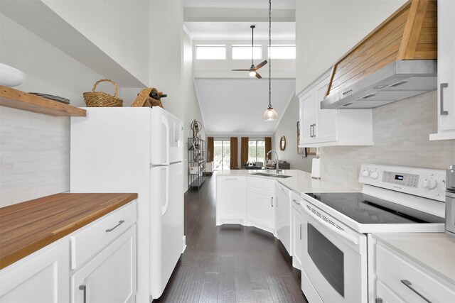 kitchen featuring white appliances, sink, wall chimney range hood, white cabinetry, and hanging light fixtures