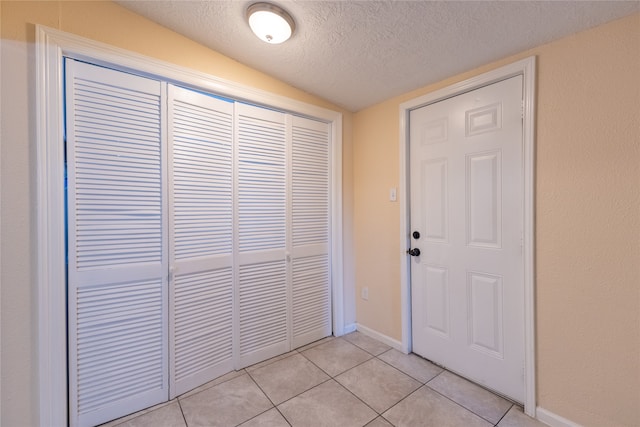 entryway with a textured ceiling, lofted ceiling, and light tile patterned flooring