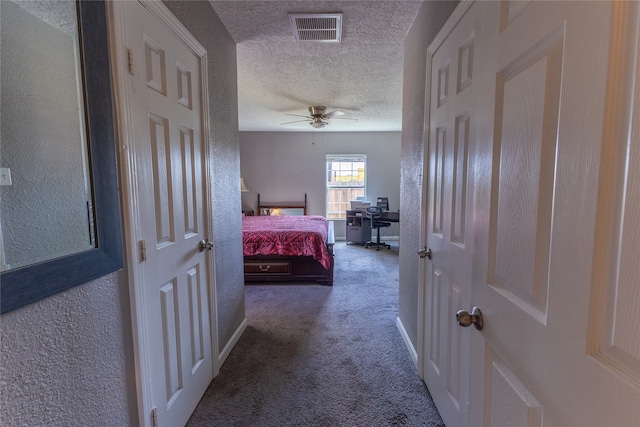 hall with a textured ceiling and dark colored carpet