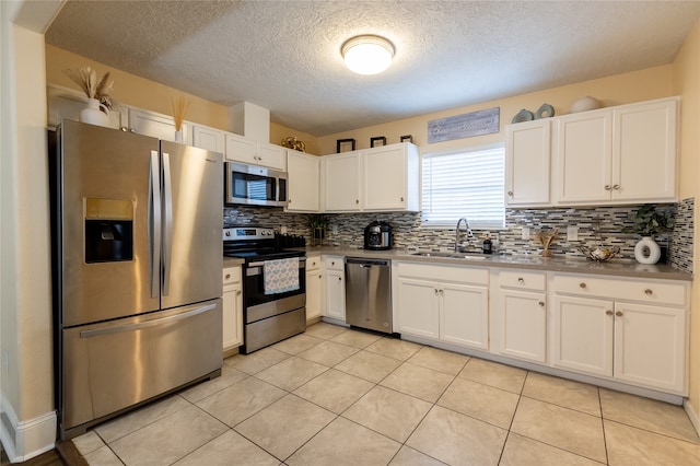 kitchen with sink, decorative backsplash, light tile patterned floors, white cabinetry, and stainless steel appliances