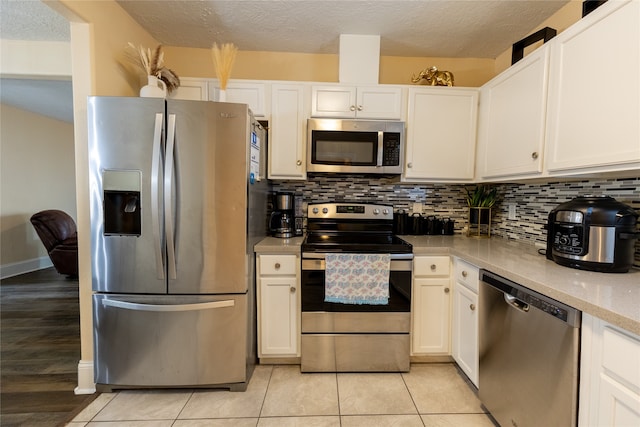 kitchen featuring appliances with stainless steel finishes, light tile patterned floors, tasteful backsplash, and white cabinetry