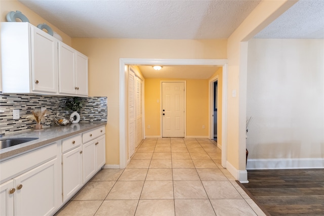 kitchen featuring white cabinets, light hardwood / wood-style floors, a textured ceiling, and tasteful backsplash