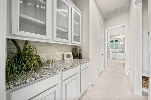 bar with white cabinets, light stone countertops, and tasteful backsplash