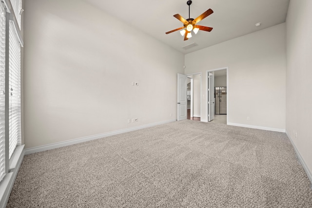 carpeted empty room with a towering ceiling, plenty of natural light, and ceiling fan