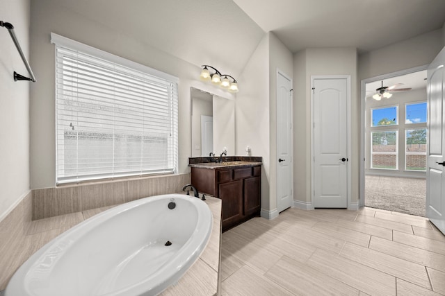 bathroom featuring ceiling fan, vanity, a healthy amount of sunlight, and a relaxing tiled tub