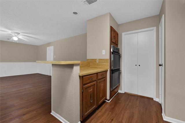 kitchen featuring a kitchen bar, kitchen peninsula, double oven, ceiling fan, and dark hardwood / wood-style floors