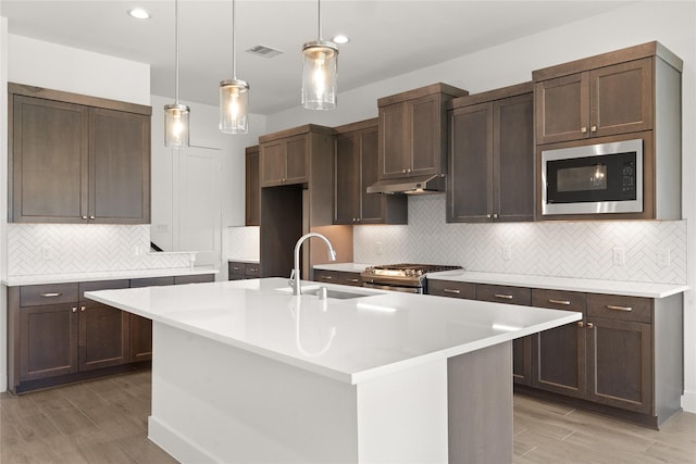 kitchen with stainless steel range with gas cooktop, built in microwave, an island with sink, and light hardwood / wood-style floors