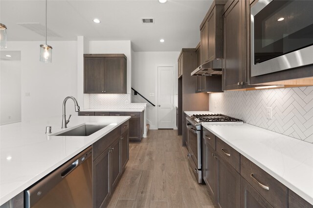 kitchen featuring decorative backsplash, stainless steel appliances, sink, light hardwood / wood-style floors, and hanging light fixtures