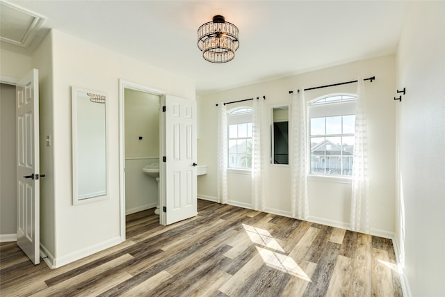 unfurnished bedroom with ensuite bath, a chandelier, and wood-type flooring