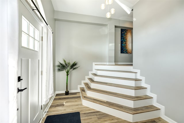 stairs featuring wood-type flooring and an inviting chandelier