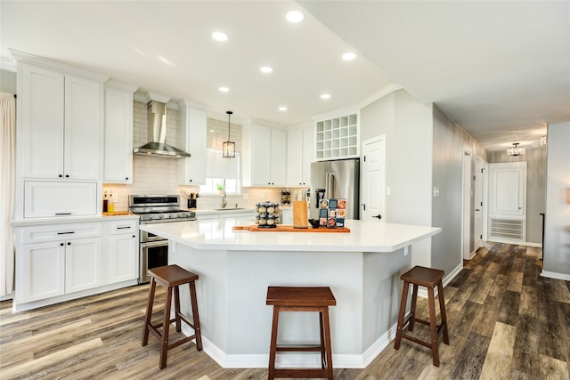 kitchen featuring white cabinetry, wall chimney exhaust hood, hanging light fixtures, dark wood-type flooring, and stainless steel appliances