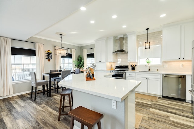 kitchen with decorative light fixtures, sink, wall chimney range hood, and stainless steel appliances