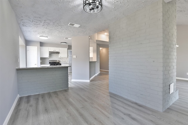 kitchen with kitchen peninsula, light stone counters, a textured ceiling, light hardwood / wood-style flooring, and white cabinetry