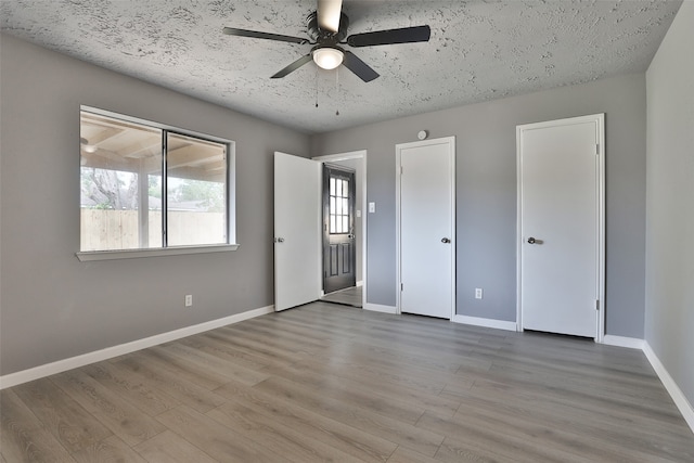 unfurnished bedroom featuring ceiling fan, multiple closets, a textured ceiling, and light hardwood / wood-style flooring