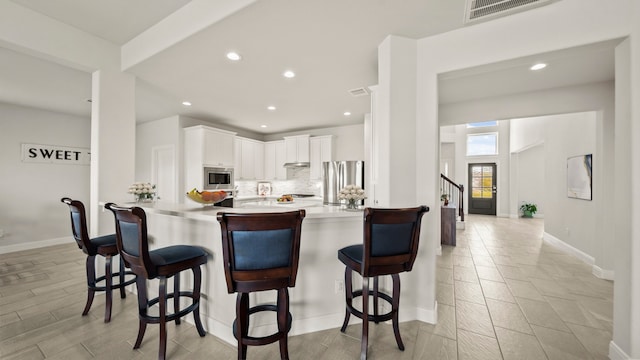 kitchen featuring kitchen peninsula, a kitchen breakfast bar, decorative backsplash, stainless steel appliances, and white cabinetry