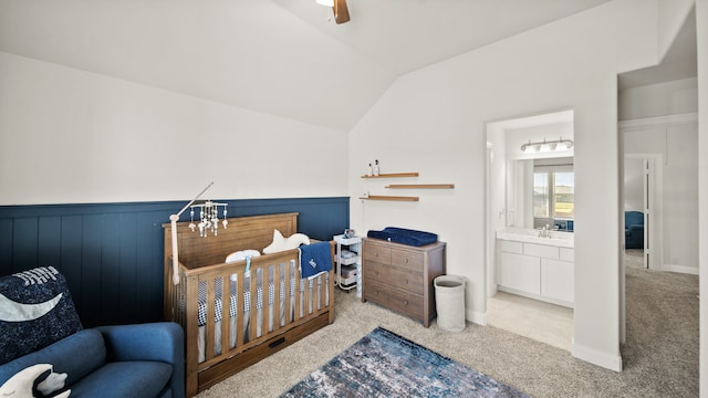 bedroom with ensuite bath, light colored carpet, vaulted ceiling, ceiling fan, and wooden walls