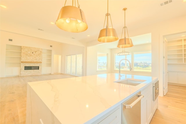 kitchen with white cabinetry, stainless steel appliances, hanging light fixtures, light stone counters, and sink