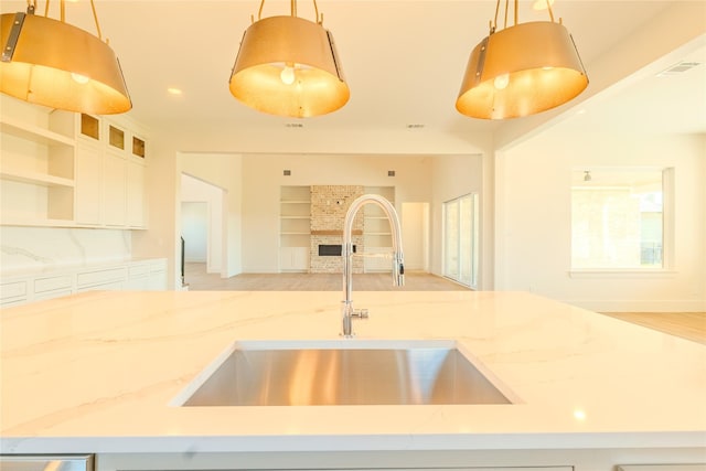 kitchen with a brick fireplace, built in features, light stone countertops, pendant lighting, and sink