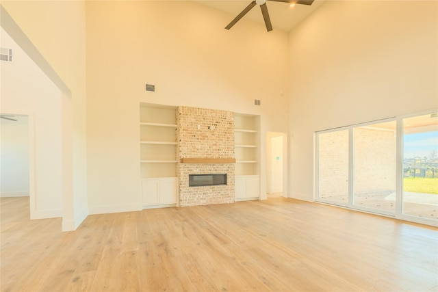 unfurnished living room featuring ceiling fan, a fireplace, a towering ceiling, light hardwood / wood-style flooring, and built in features