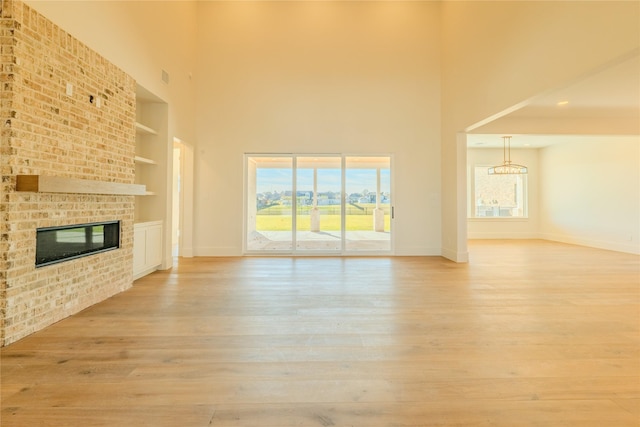 unfurnished living room featuring built in shelves, a fireplace, a towering ceiling, and light hardwood / wood-style floors