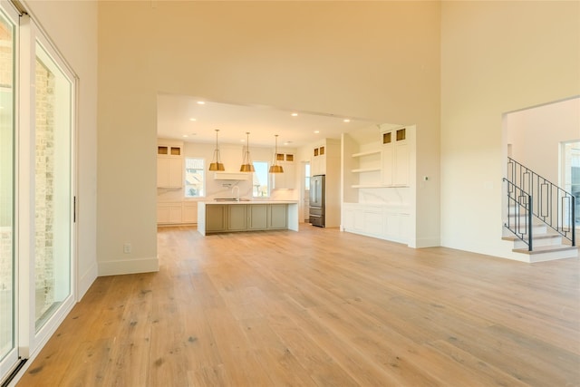 unfurnished living room featuring a towering ceiling, light hardwood / wood-style flooring, and sink