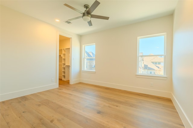 empty room with ceiling fan, a wealth of natural light, and light wood-type flooring