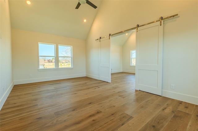 empty room with high vaulted ceiling, plenty of natural light, a barn door, and light wood-type flooring