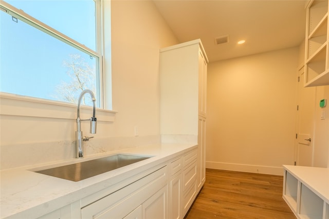 kitchen with hardwood / wood-style floors, white cabinetry, light stone counters, and sink