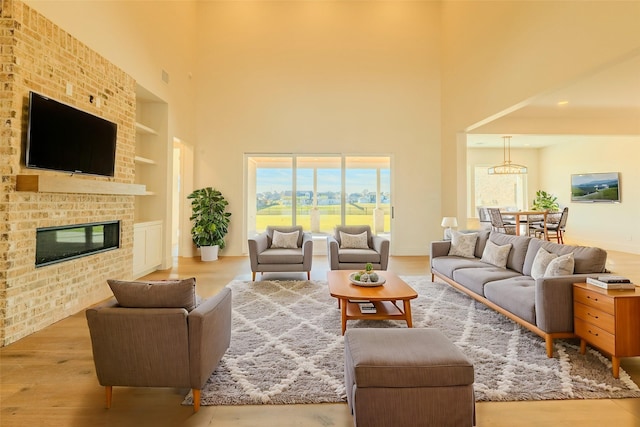 living room featuring built in shelves, a fireplace, a towering ceiling, and light hardwood / wood-style floors