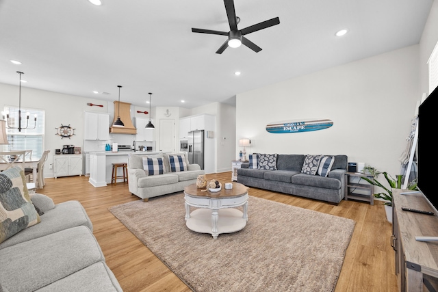 living room featuring ceiling fan with notable chandelier and light hardwood / wood-style flooring