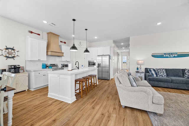 kitchen featuring an island with sink, a breakfast bar area, white cabinets, custom exhaust hood, and stainless steel appliances