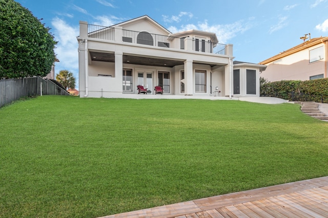 rear view of property featuring french doors, a balcony, and a lawn