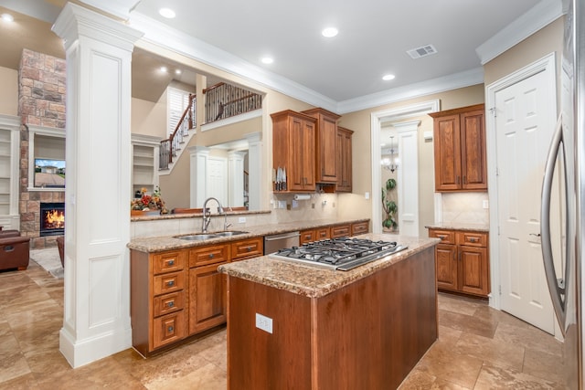 kitchen featuring ornamental molding, stainless steel appliances, sink, a fireplace, and a center island