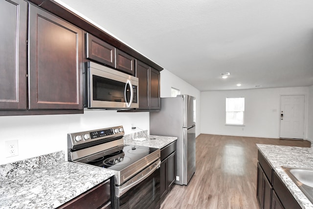 kitchen with light wood-type flooring, light stone counters, dark brown cabinetry, stainless steel appliances, and sink