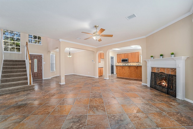 unfurnished living room featuring a tile fireplace, crown molding, and ceiling fan