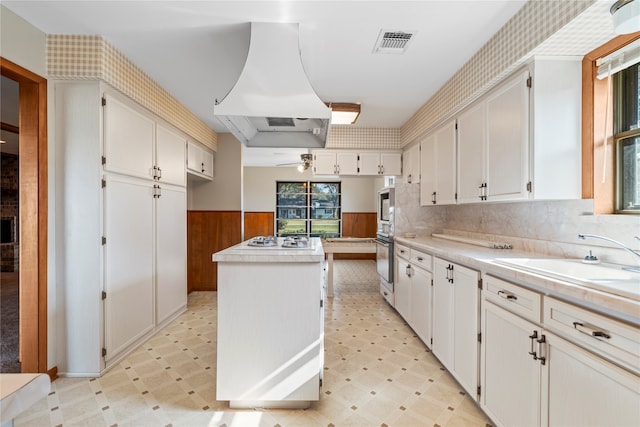 kitchen with white cabinetry, a kitchen island, white gas stovetop, and ventilation hood