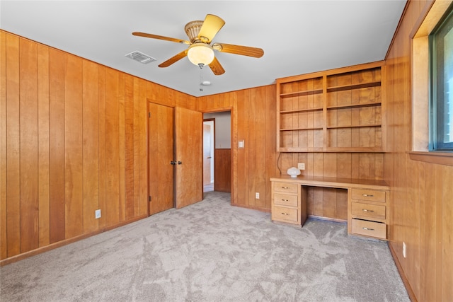 unfurnished office featuring ceiling fan, light carpet, built in features, wooden walls, and built in desk